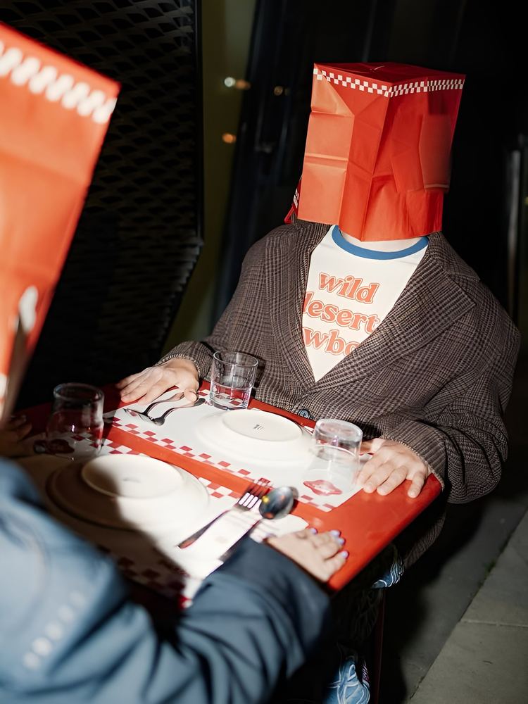 Two diners with paper bags over their heads at a red gingham table