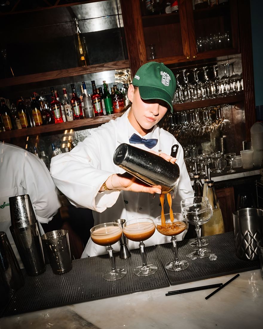 A bartender pouring espresso martinis along a bar