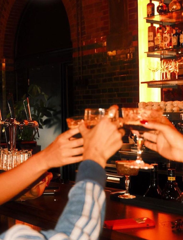 Friends raising cocktails at a lit back bar