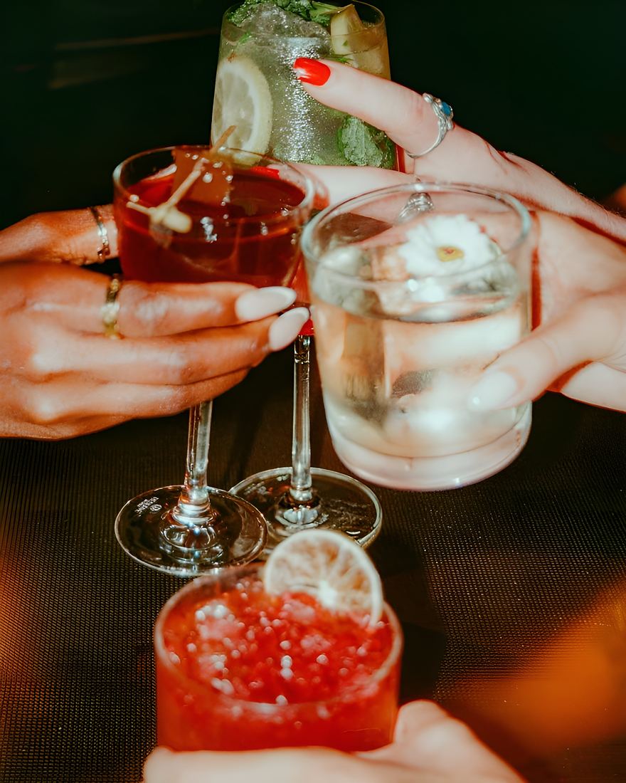 Hands holding cocktails across a bar table on film