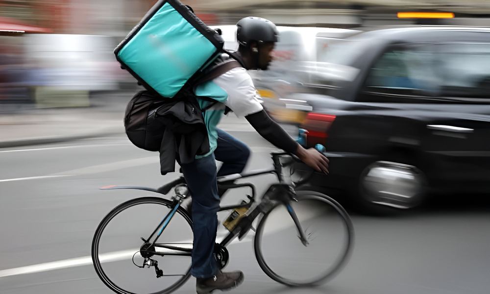 A delivery cyclist in motion past a black cab