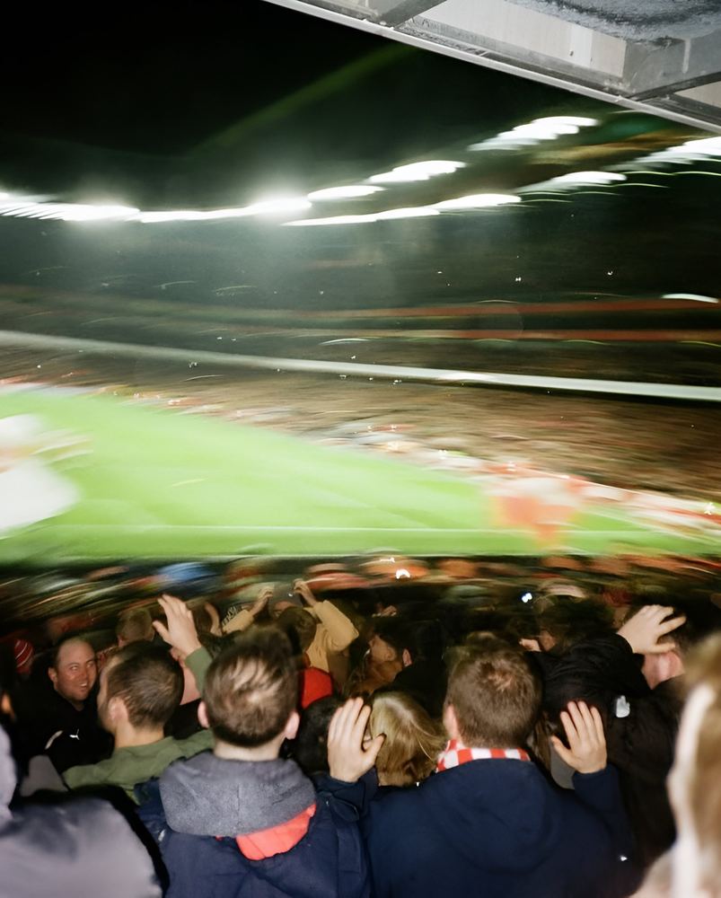 Fans in a stand under floodlights, blurred